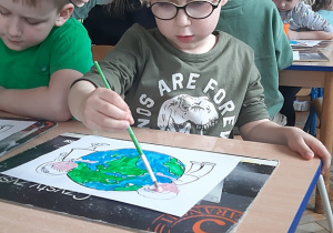 Eryk maluje farbami plakatowymi planetę Ziemię.